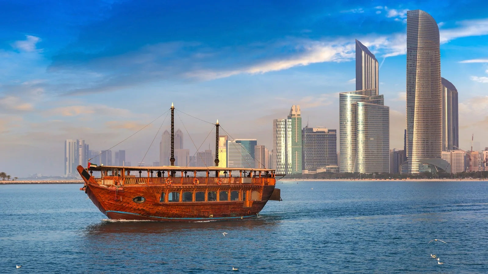 Dhow boat sailing on the Arabian Gulf near Abu Dhabi Corniche with modern skyscrapers and waterfront views