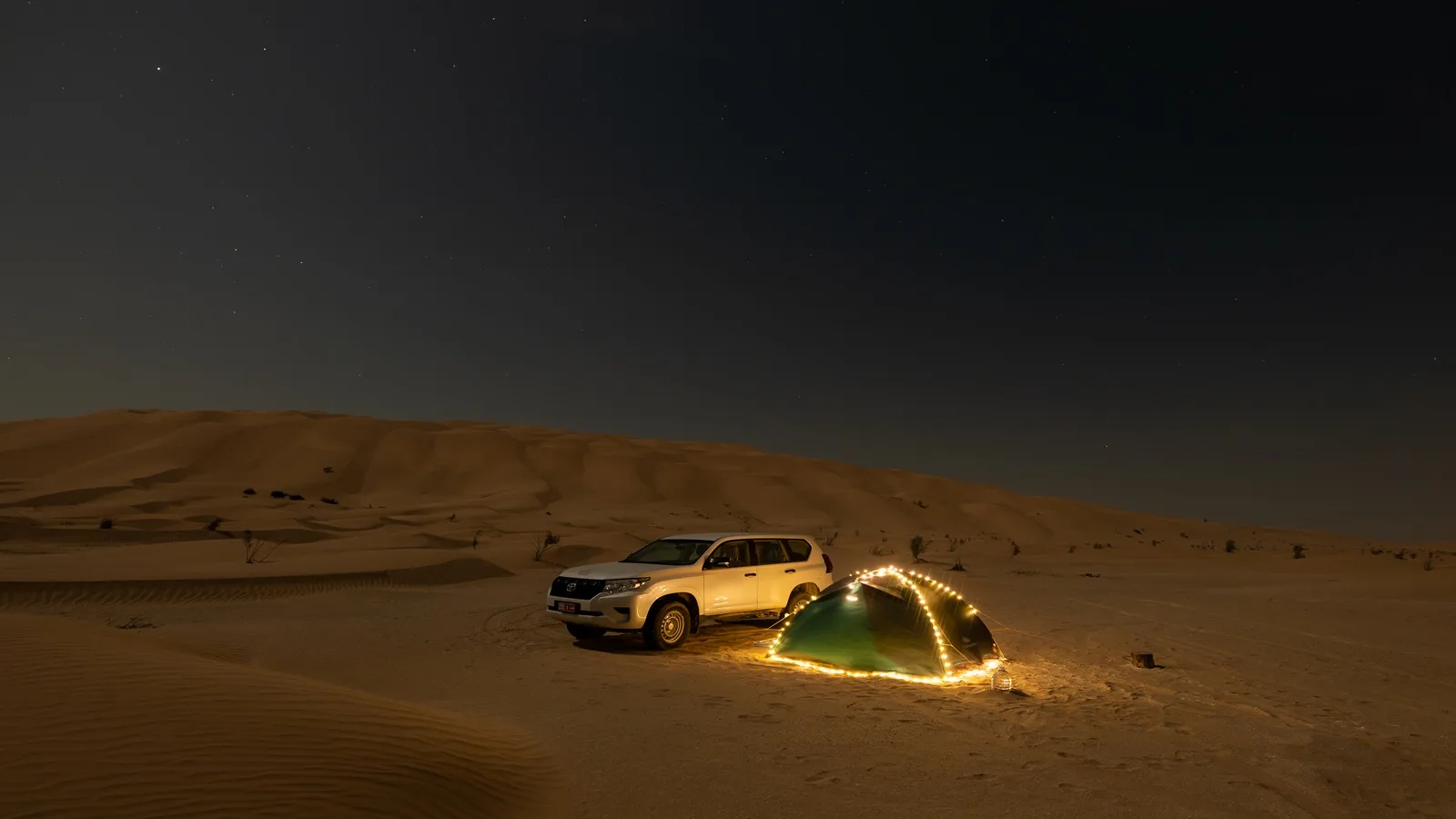 Traditional desert camping tent surrounded by golden dunes under the Arabian night sky