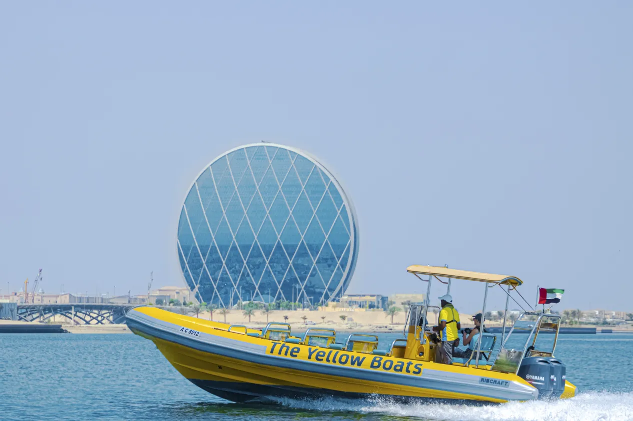 Yellow Boat Tour cruising near the iconic coin-shaped Aldar Headquarters building in Abu Dhabi