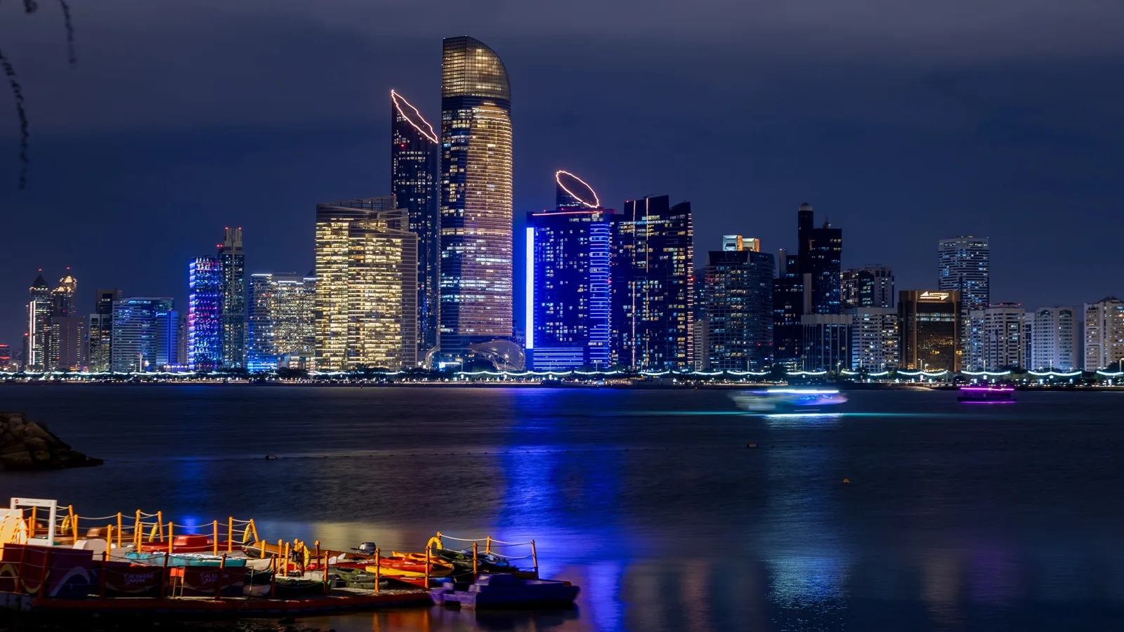 Abu Dhabi skyline illuminated at night, with modern skyscrapers reflecting across the waterfront