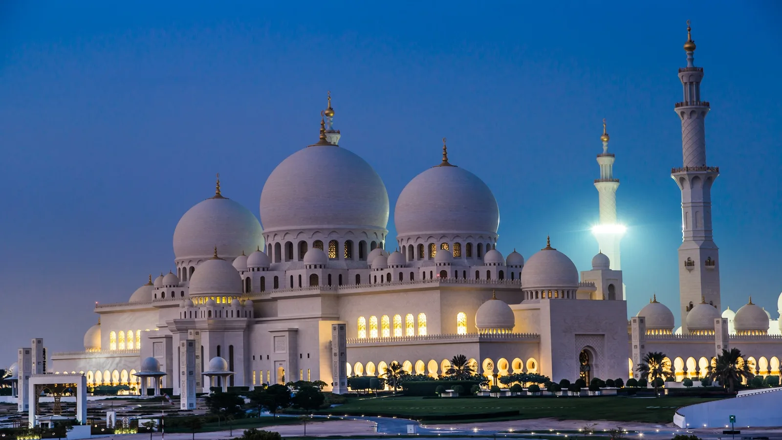 Sheikh Zayed Grand Mosque illuminated in the evening, with its white domes and minarets reflected in the surrounding pools
