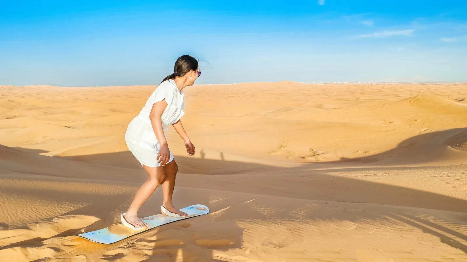 Tourist sandboarding down golden desert dunes during a Half Day Desert Safari in Abu Dhabi