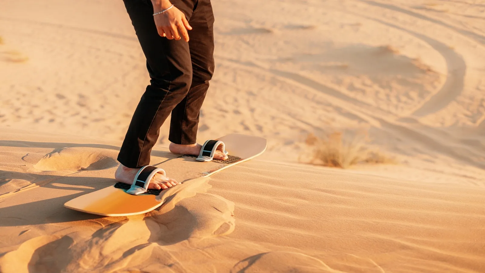 Tourist sandboarding down golden sand dunes during a Sunrise Desert Safari in Abu Dhabi
