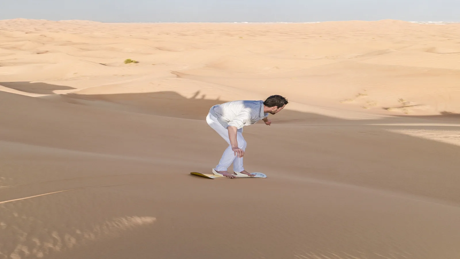 Tourist sandboarding down the golden dunes during a Morning Desert Safari in Abu Dhabi