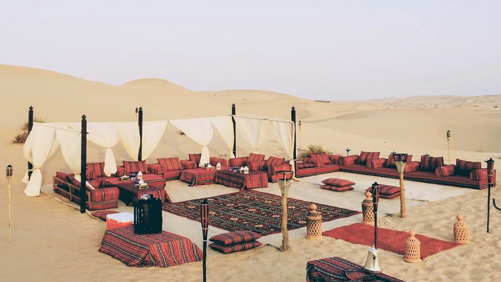 Private romantic dinner setup with cushions, low table, lanterns, and soft lighting surrounded by golden desert dunes