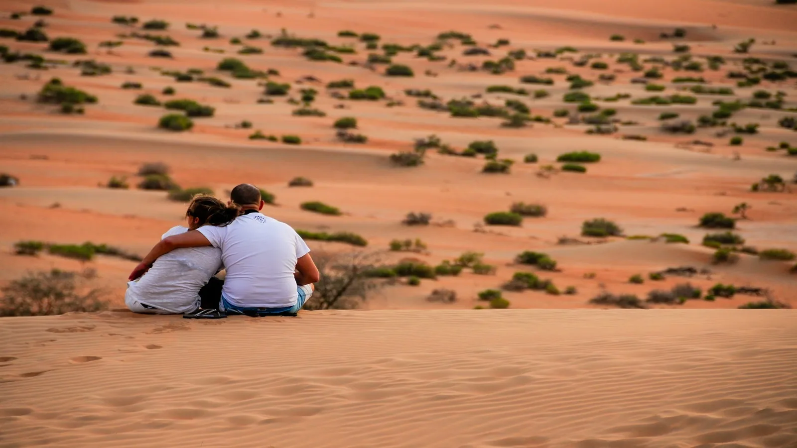 Couple sitting together on a romantic desert setup surrounded by golden dunes during sunset