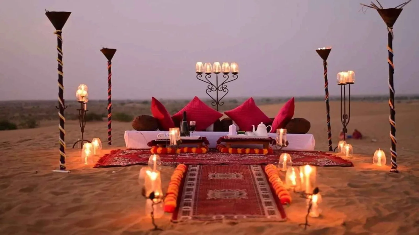 Romantic private dune dinner setup with comfortable seating, dining table, lanterns, and decorations in the Abu Dhabi desert