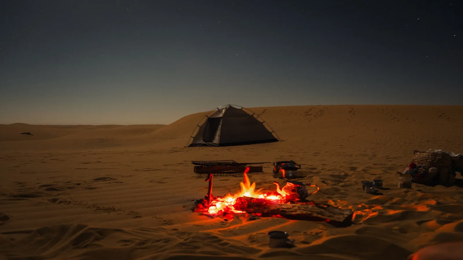 Overnight desert safari tent illuminated by a warm campfire among the golden dunes at night